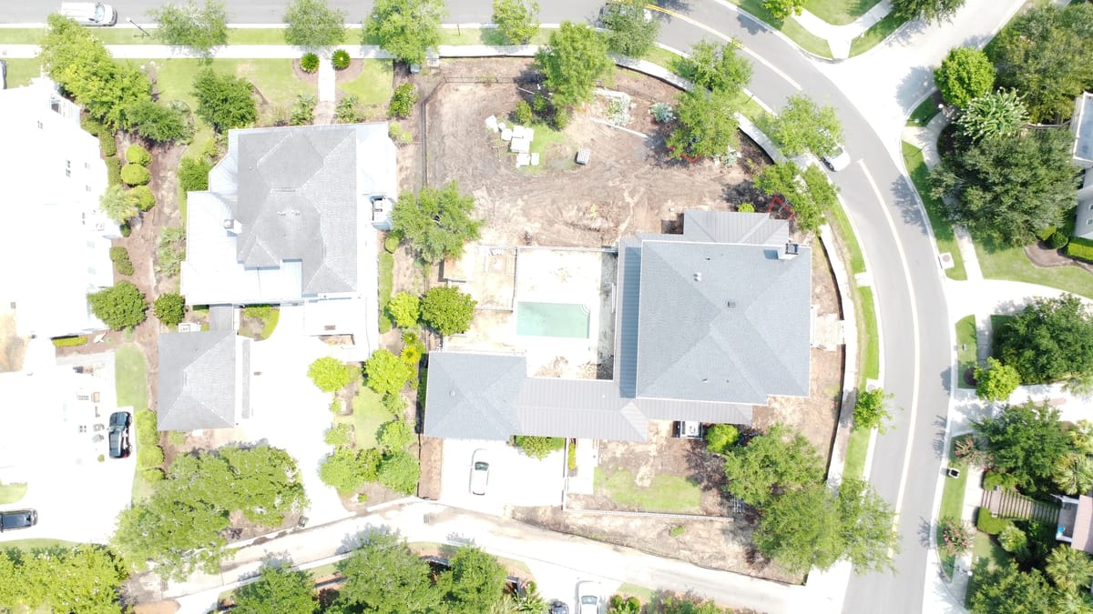 Aerial view of houses with gray roofs, green lawns, and a partially cleared yard.