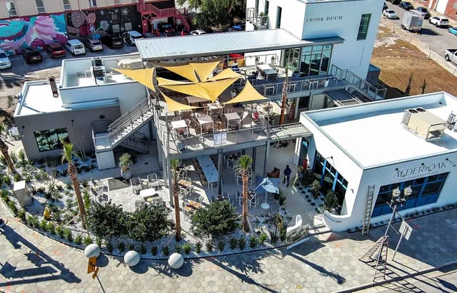 Exterior view with rooftop terrace, tan canopies, outdoor seating, palm trees, and landscaping.