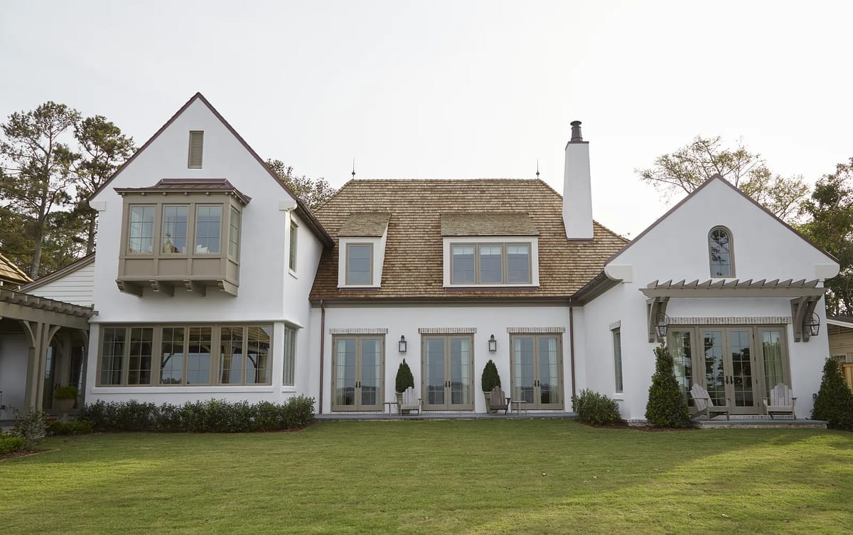 House exterior with sloped roof, multiple windows, deck, lawn, and potted plants.