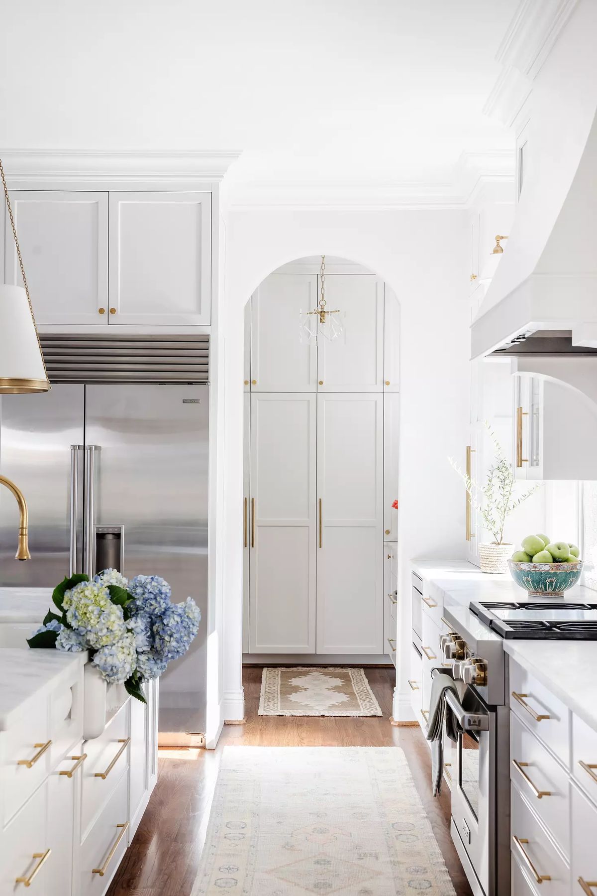 Kitchen with stainless steel appliances, white cabinetry, marble countertop, arched doorway, and decorative bowl of apples.