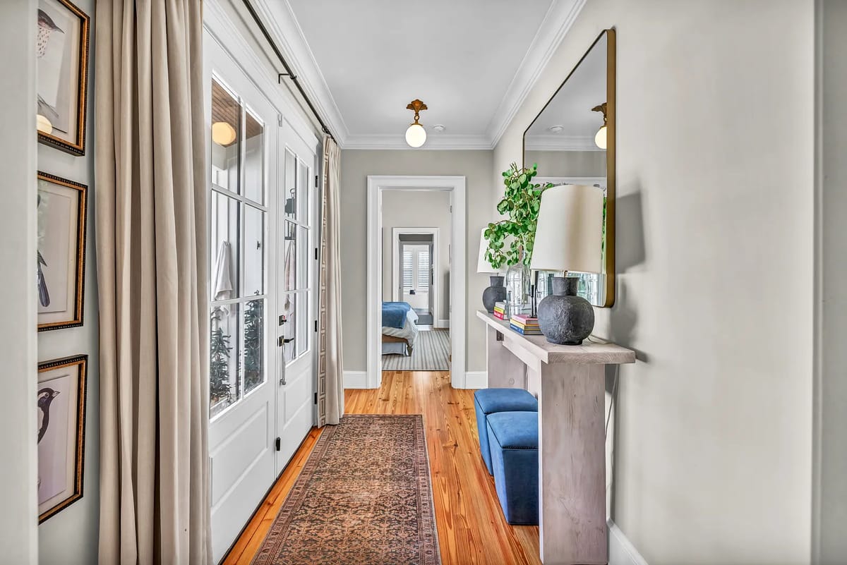 Hallway with a console table, lamp, mirror, framed artwork, and wood flooring.