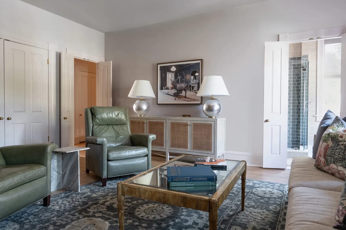 Living room with green armchairs, glass coffee table, patterned rug, sofa, artwork, and double doors.