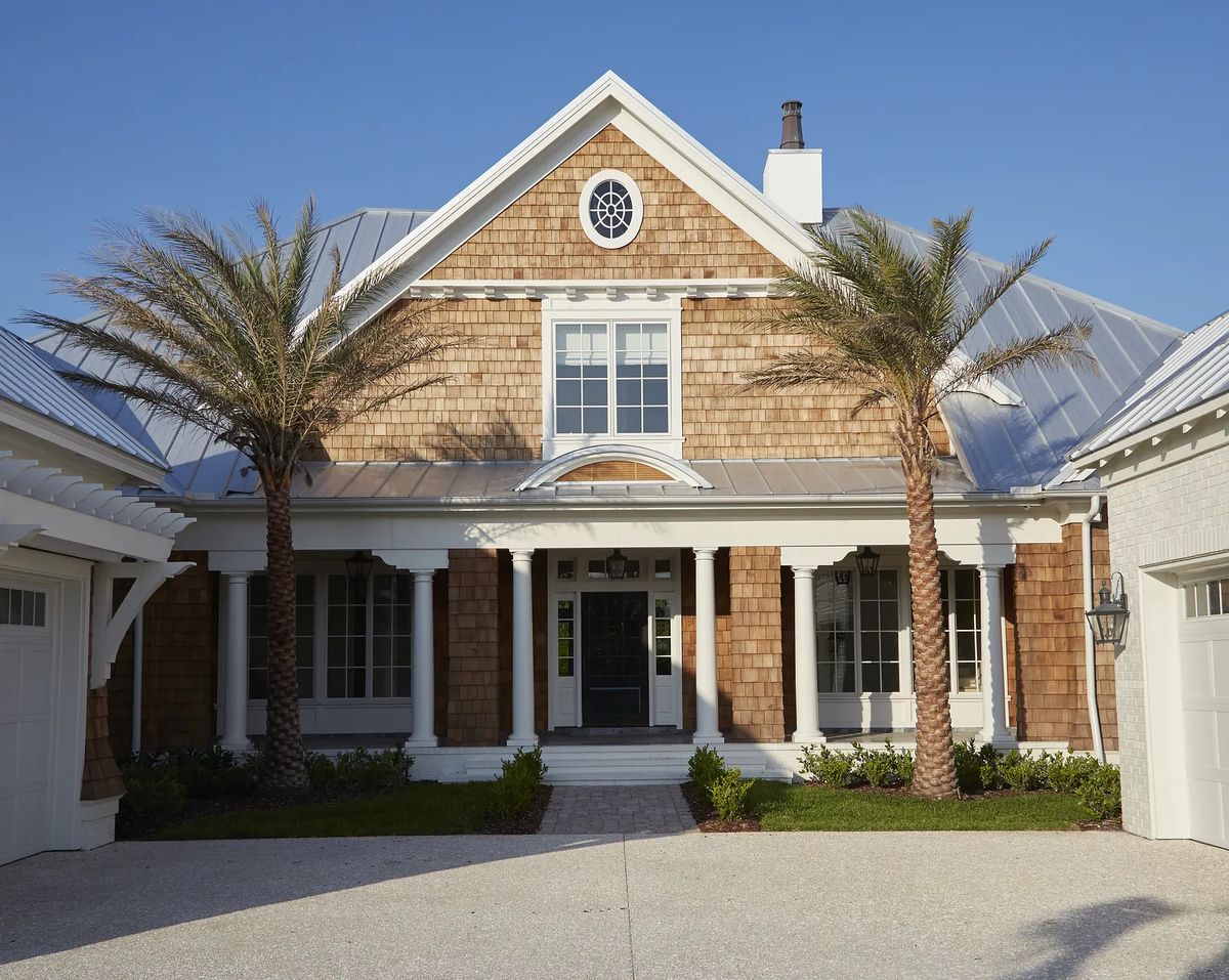 Front exterior of a house with gable roof, wood shingles, central entrance, and palm trees.