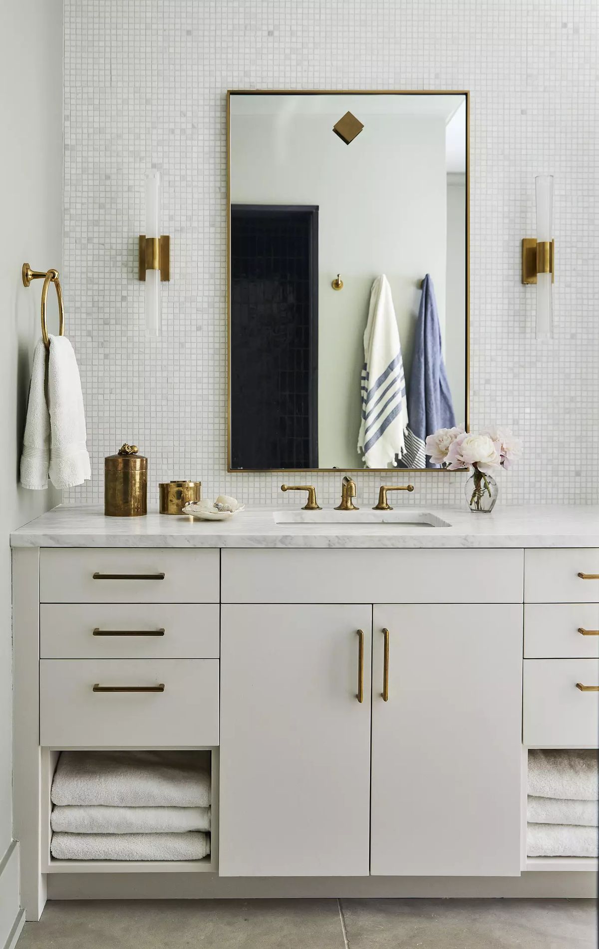 Bathroom with white vanity, gold hardware, large mirror, wall sconces, and beige tiled flooring.