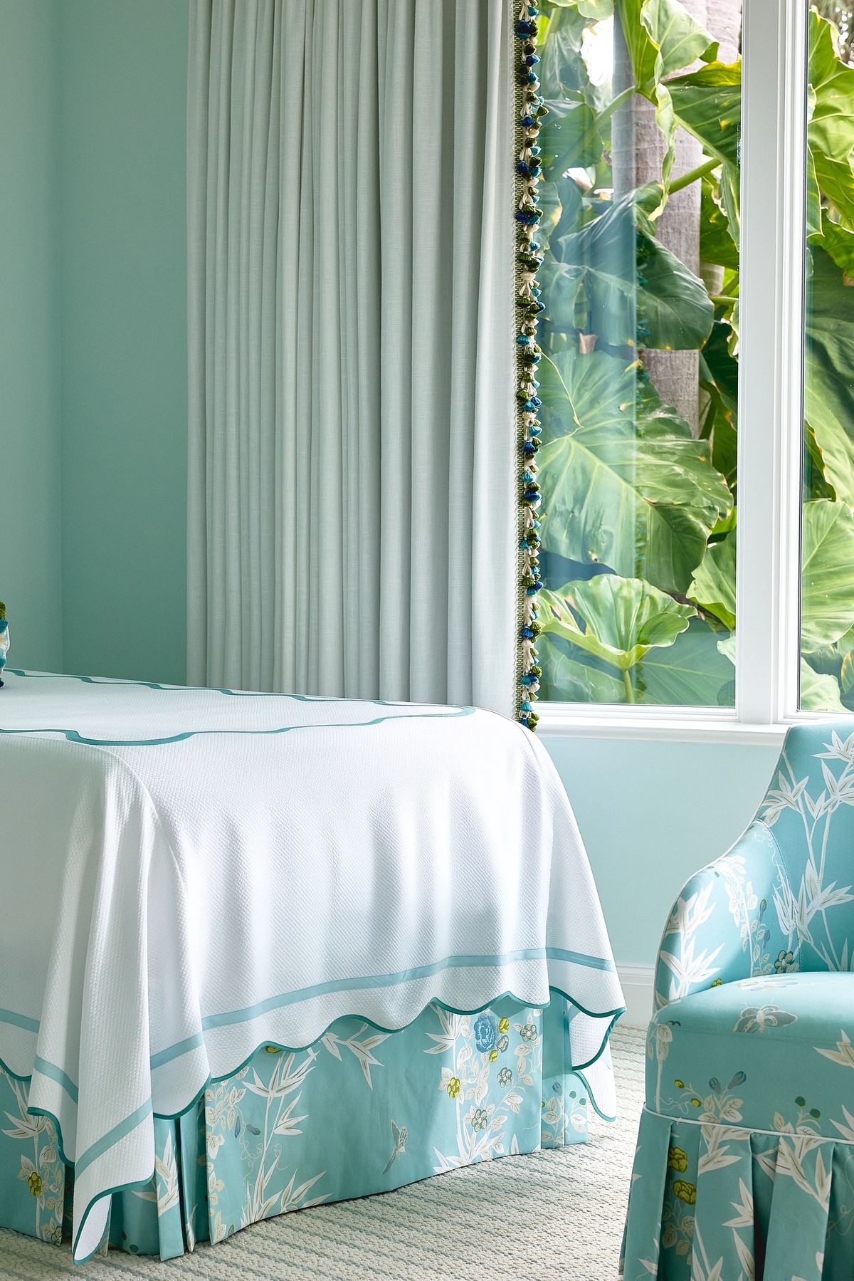 Bedroom with bed, floral chair, large windows, sheer curtains, and light teal walls