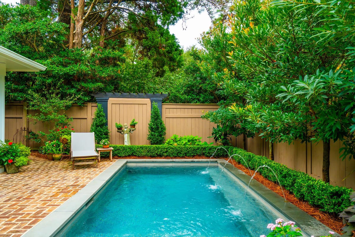 Outdoor area with a swimming pool, brick pavers, lounge chair, plants, and water features.