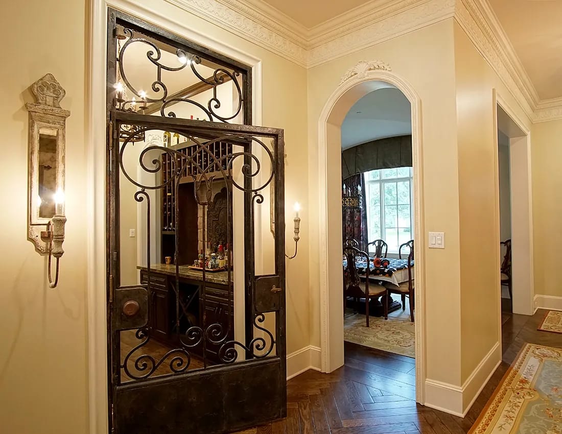 Foyer with wrought iron gate, beige walls, herringbone wood floor, and archway to another room.