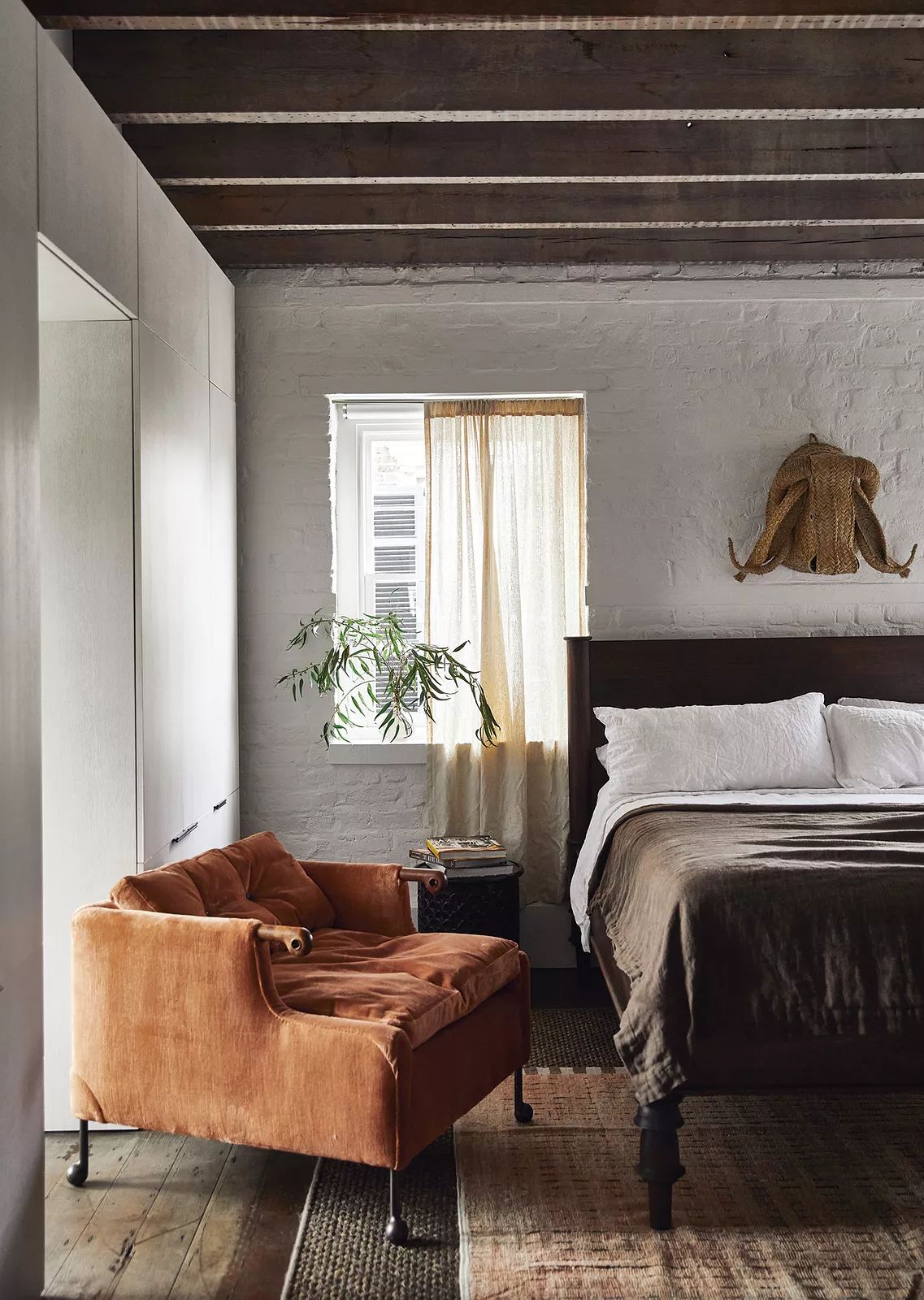 Bedroom with brown bed, orange velvet chair, wooden nightstand, and exposed wooden beams