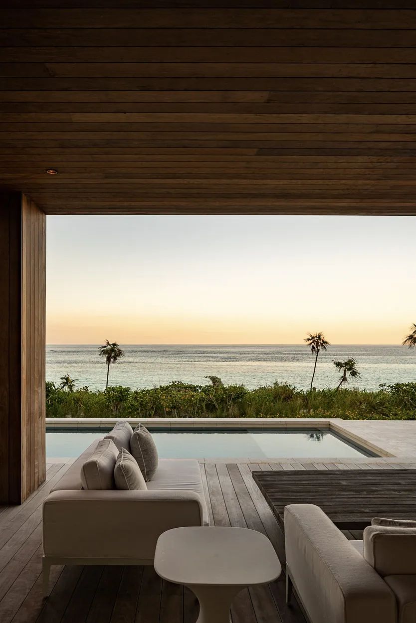 Outdoor deck with white sofas, table, and ocean view with palm trees.