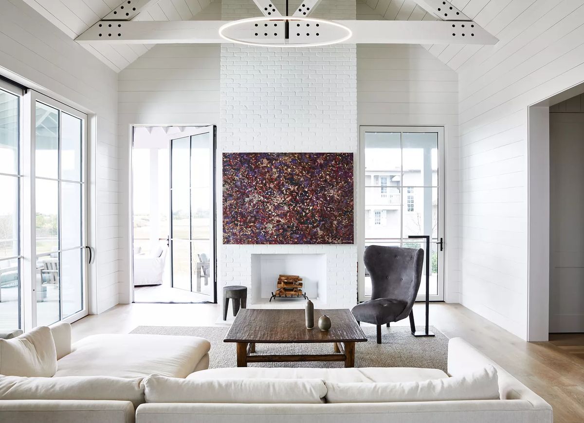 Living room with white sofa, wood coffee table, gray chair, large painting, and multiple glass doors.