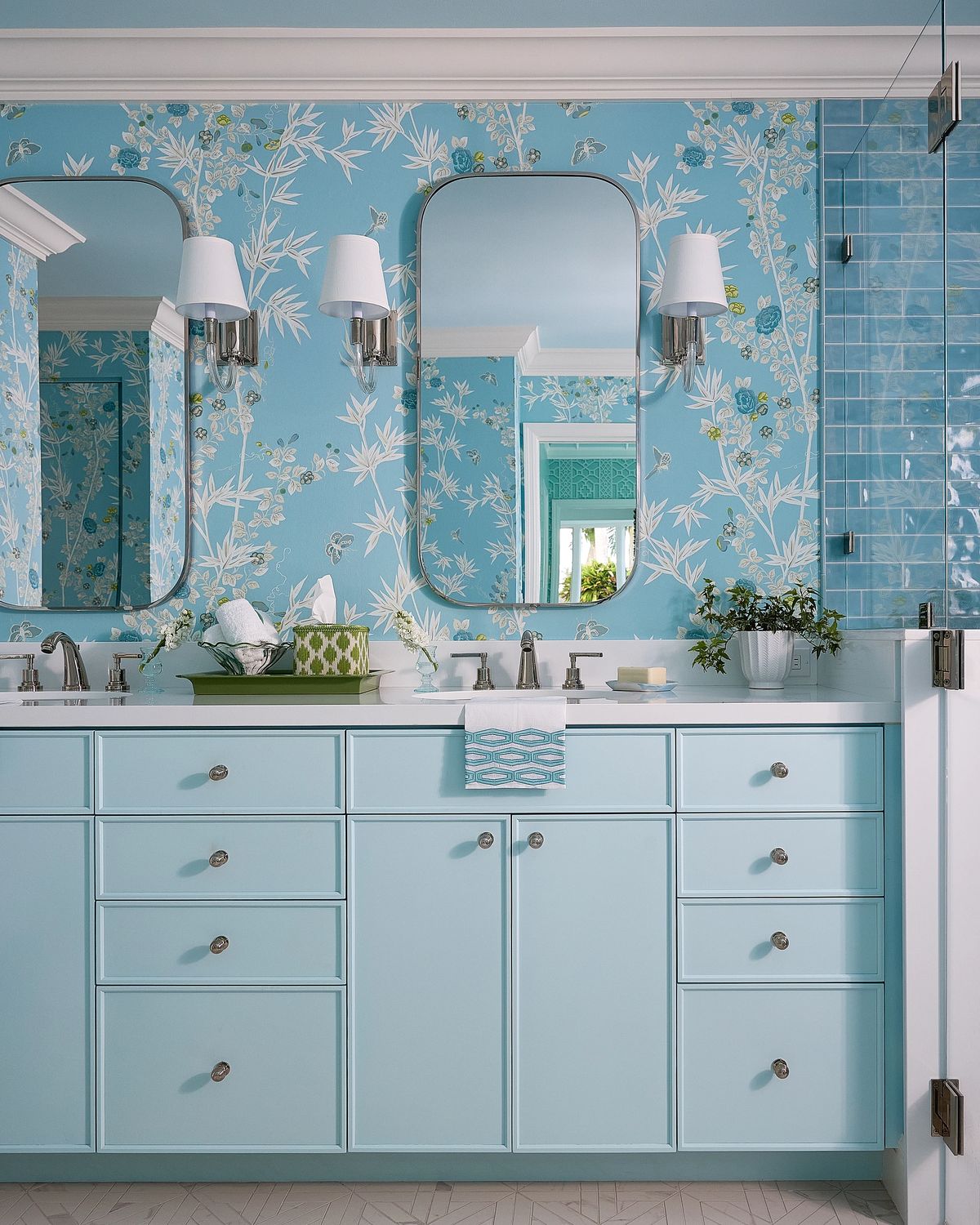 Bathroom with light blue cabinetry, double vanity, floral wallpaper, large mirrors, and glass shower enclosure