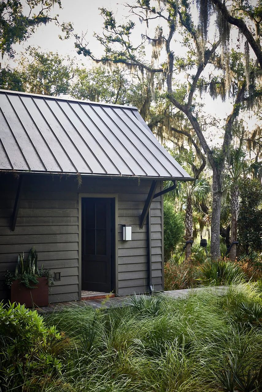 Exterior view with metal roof, wood siding, door, grass, and surrounding trees.