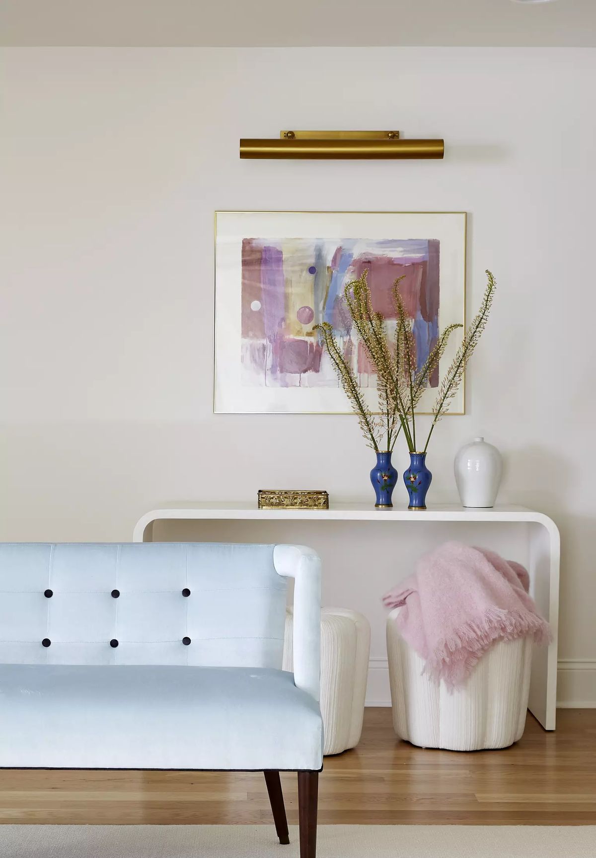 Living room with light blue sofa, white stools, console table, abstract artwork, and decorative vases with flowers.