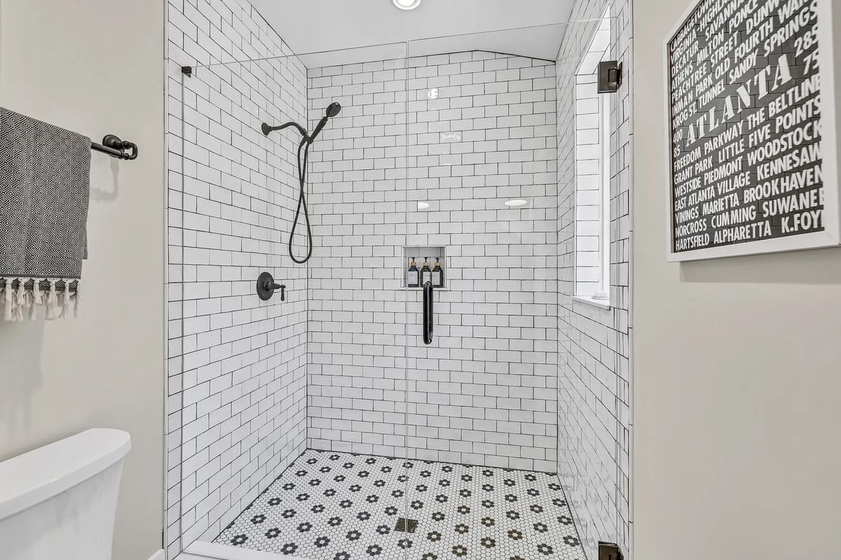 Bathroom with glass shower, white tiles, black floor tiles, towel bar, and graphic wall art.