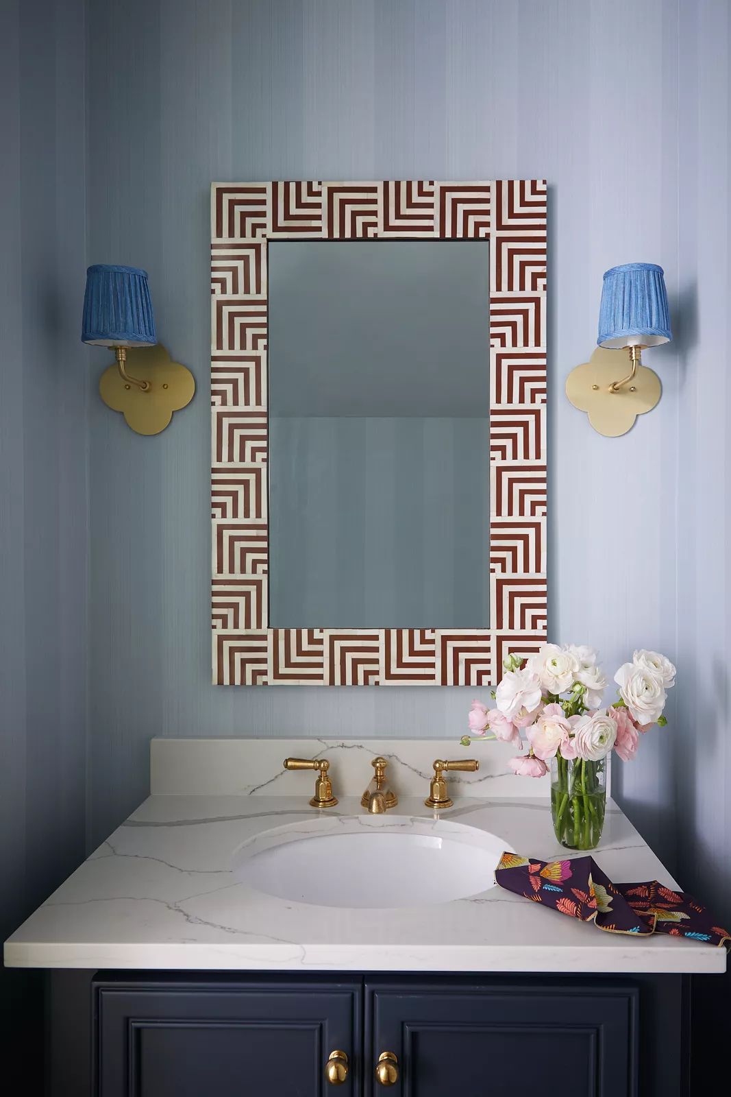 Powder room with marble countertop, brass faucet, geometric mirror, and blue walls with flowers