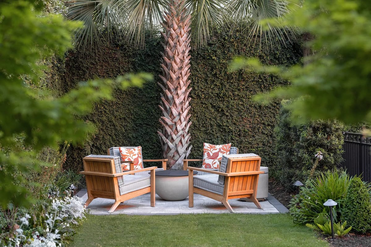 Garden space with wooden armchairs, palm tree, and surrounding greenery.