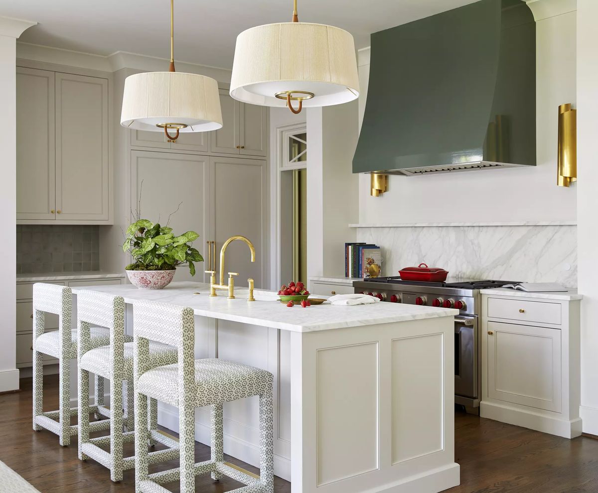 Kitchen with island, bar stools, green range hood, marble backsplash, and stainless steel appliances.