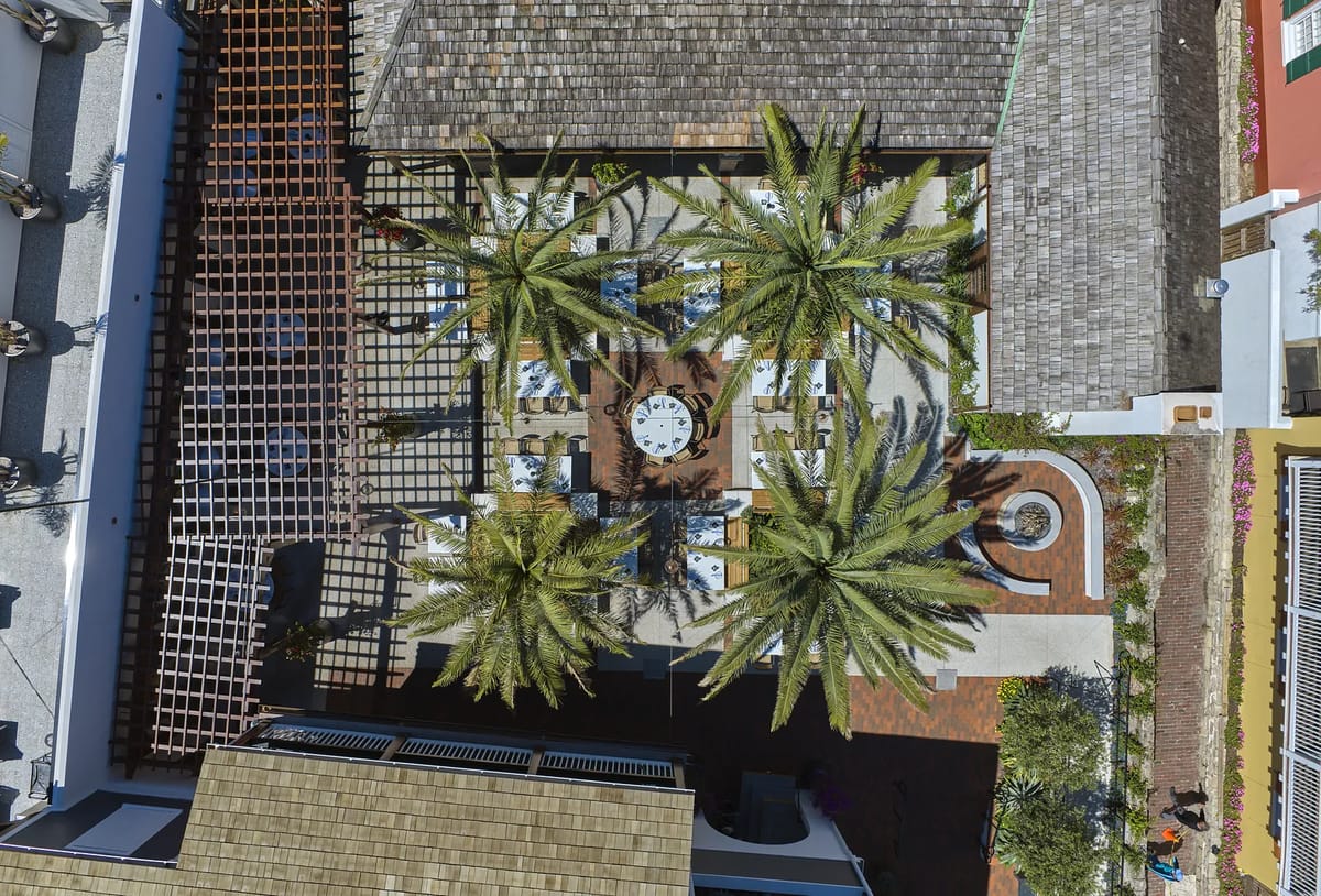 Outdoor patio with circular table, chairs, potted palms, and raised greenery.