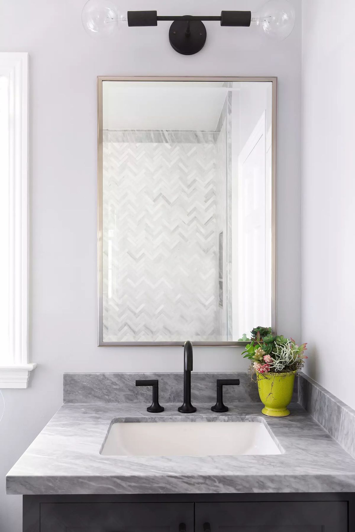 Bathroom with gray marble countertop, white sink, black faucet, mirror, and herringbone tile wall.