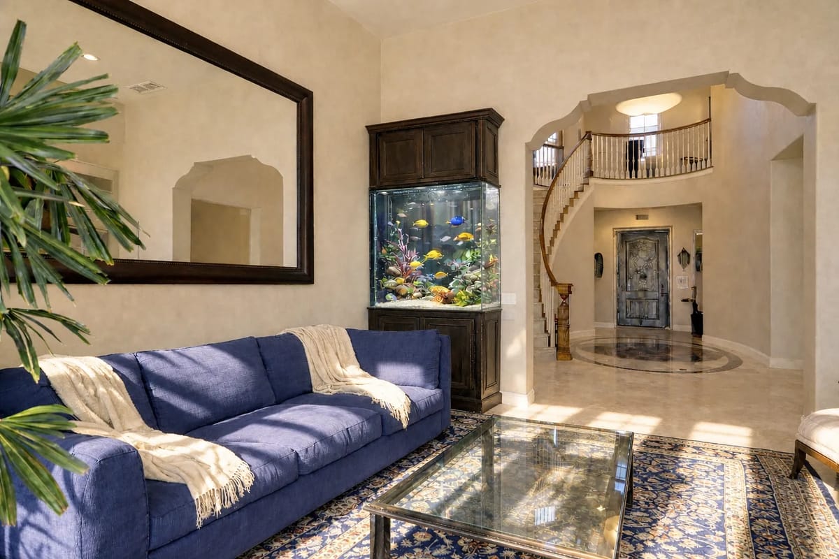 Living room with blue sofa, glass coffee table, area rug, mirror, and aquarium with staircase in the background.