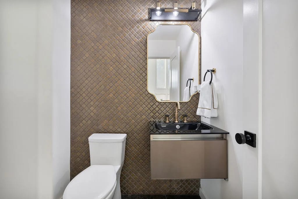 Powder room with wall-mounted sink, black granite countertop, white toilet, and textured brown tile wall.