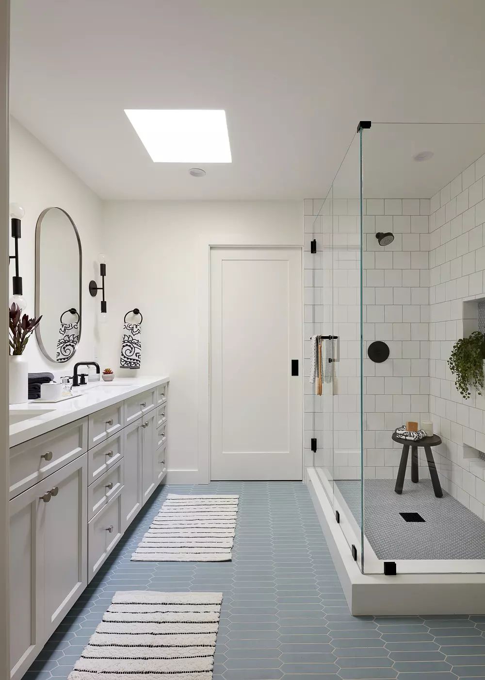 Bathroom with gray vanity, dual sinks, large mirror, glass shower, and hexagonal blue tile flooring.