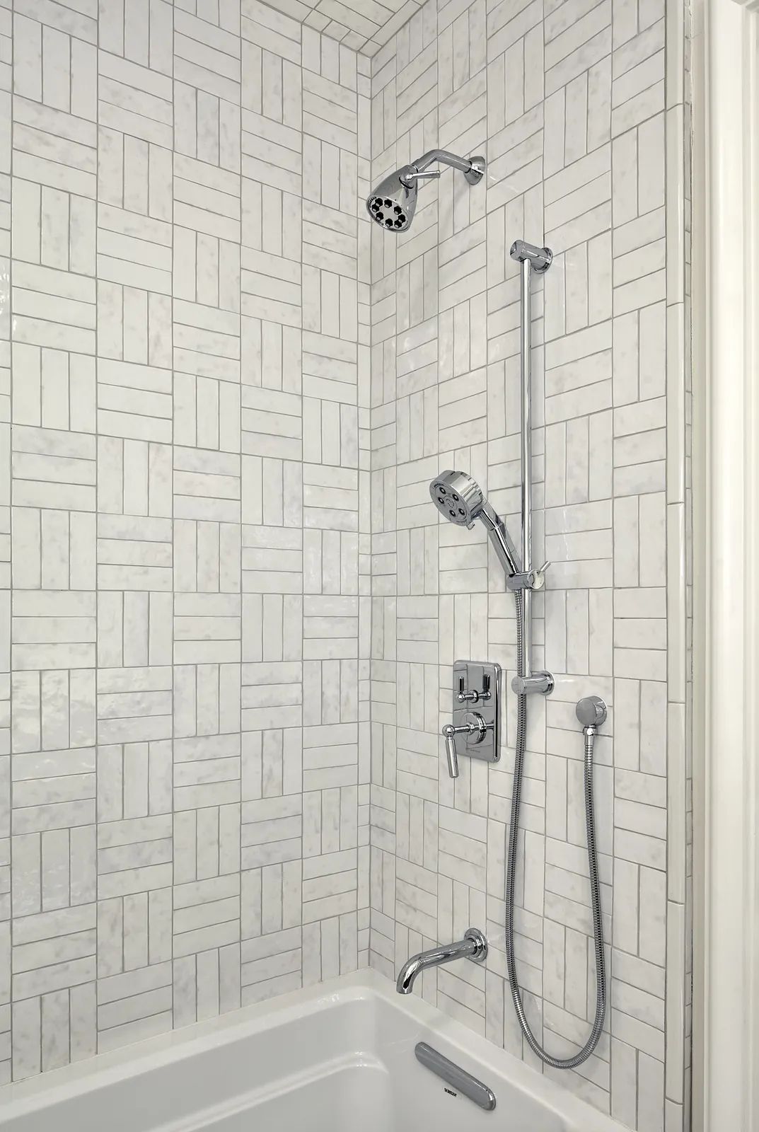 Bathroom with white bathtub, chrome faucet, and light gray tile wall