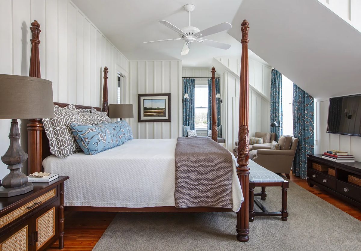 Bedroom with four-poster bed, nightstands, rug, curtains, and seating area with armchair and ottoman.