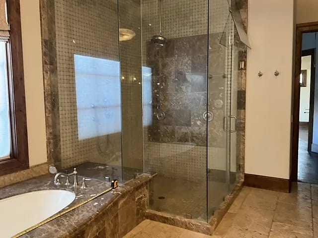 Bathroom with glass shower, soaking tub, marble countertop, and tiled walls.