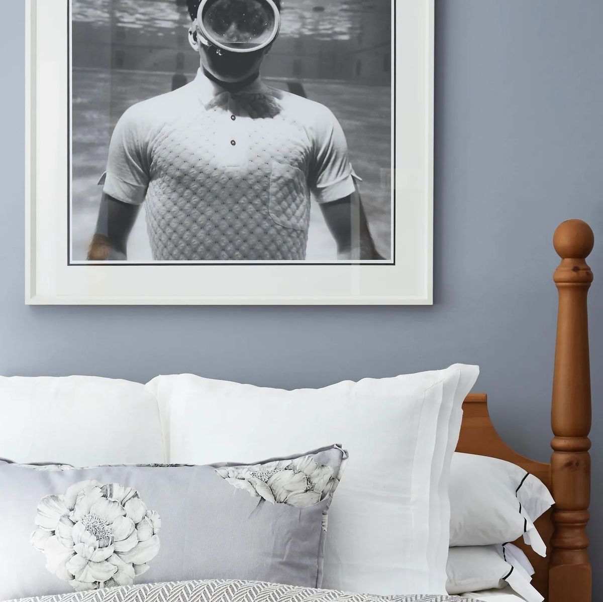 Bedroom with wooden bed frame, white bedding, decorative pillows, and framed photograph above the bed.
