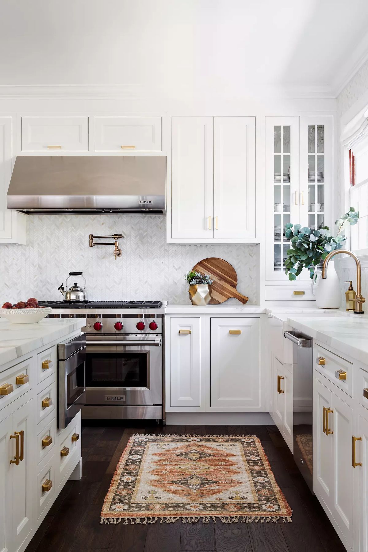 Kitchen with white cabinets, stainless steel range, herringbone backsplash, marble countertop, and decorative rug