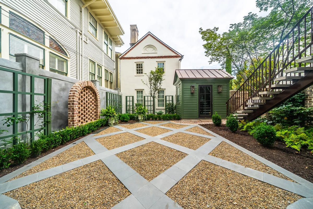 Garden with gravel pathway, plants, brick arch, green shed, and staircase leading to an upper level.