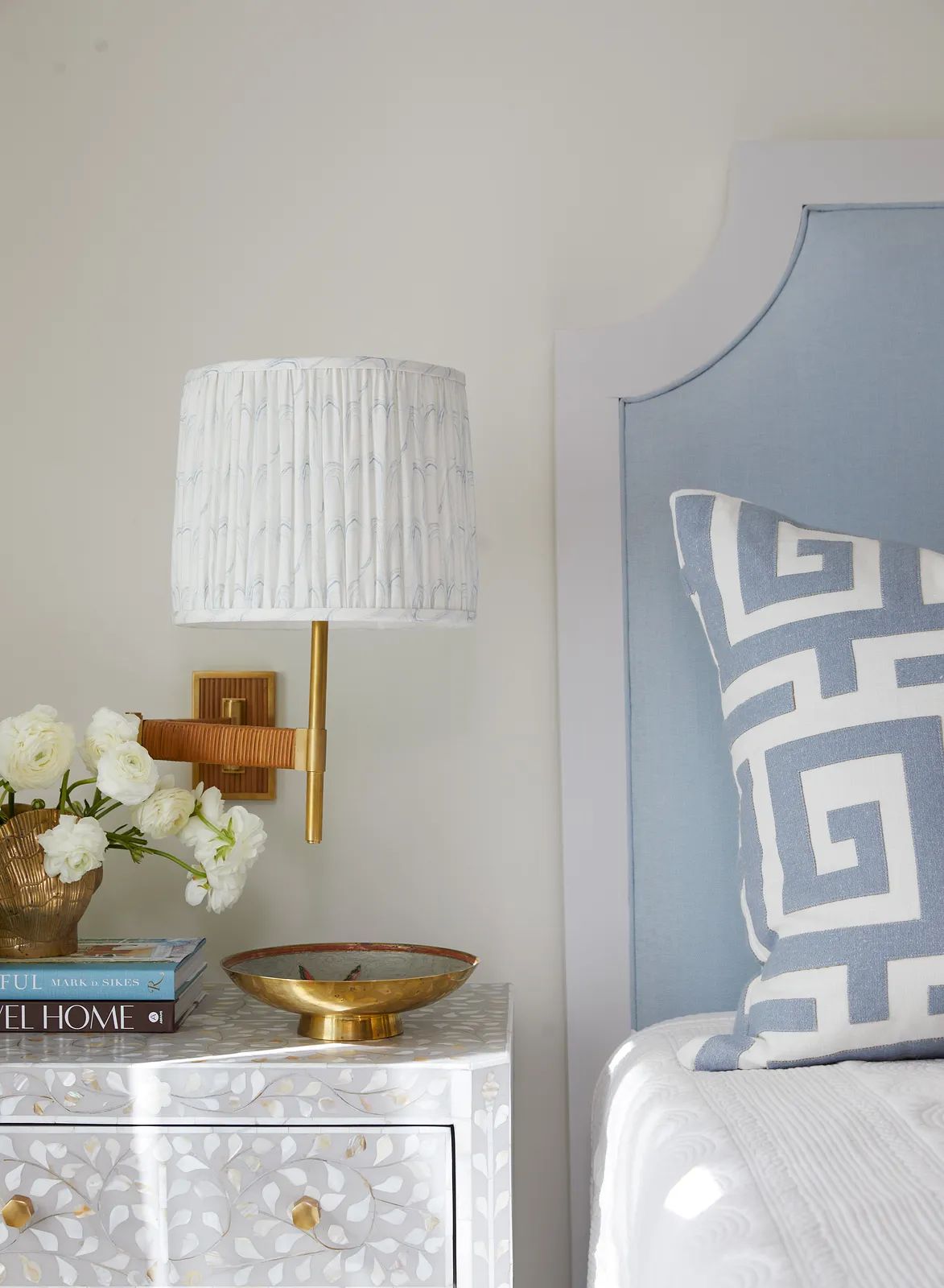 Bedroom with light blue headboard, nightstand with decorative bowl, lamp, and patterned pillow.