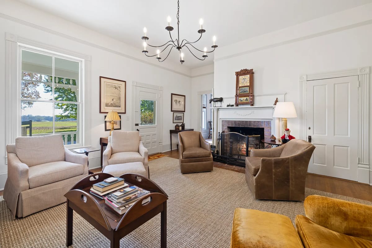 Living room with armchairs, brown sofa, coffee table, fireplace, large windows, and artwork.