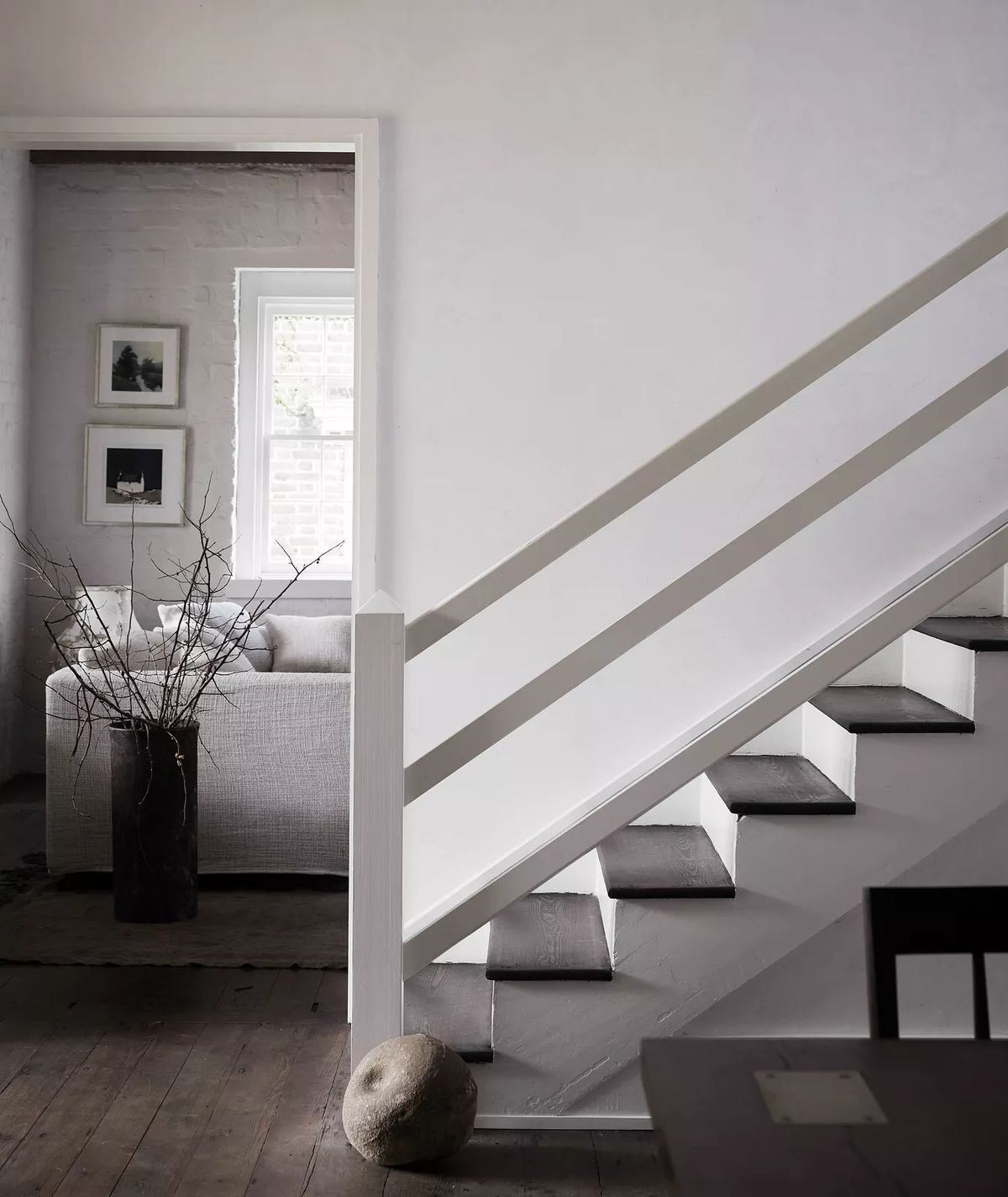 Transitional space with staircase, gray sofa in living area, and a tall vase with branches.
