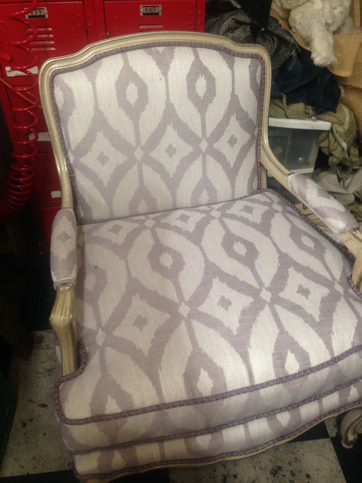 Upholstered chair with gray and lavender pattern, wooden frame, and placed on two-tone floor.