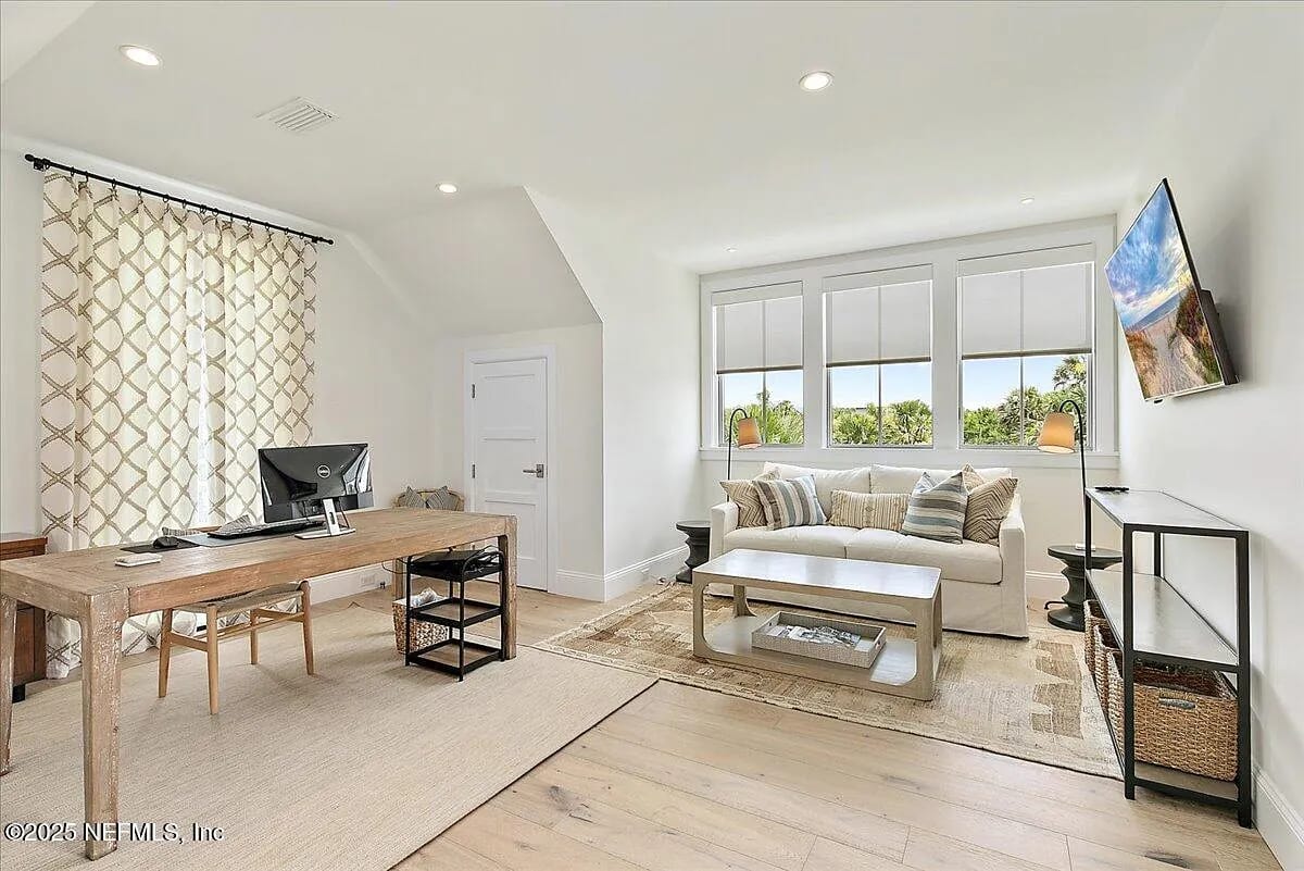 Office with wooden desk, computer, white coffee table, sofa, and large windows with gray shades