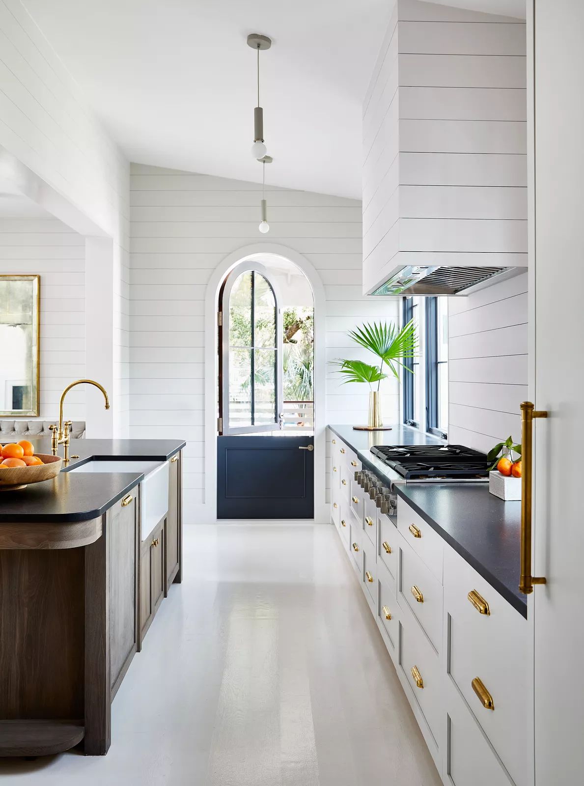 Kitchen with wood island, dark countertops, white cabinetry, arched window, and door providing natural light.