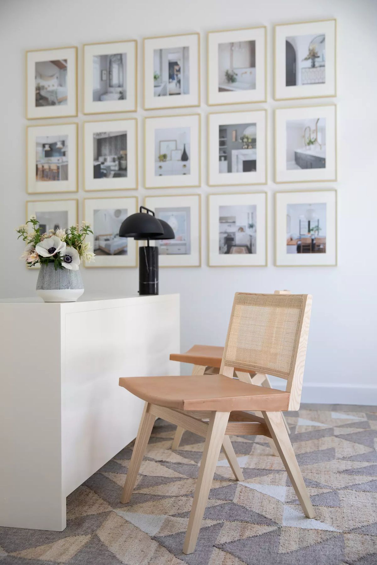 Office with light wood desk, wooden chairs, decorative vase, and a grid of framed photographs on the wall.