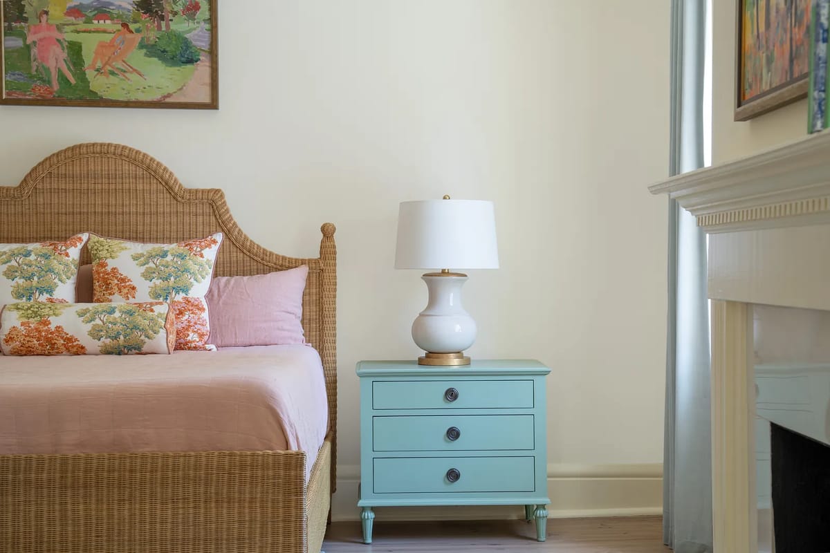 Bedroom with woven bed, pink bedspread, blue nightstand, lamp, and artwork on the walls