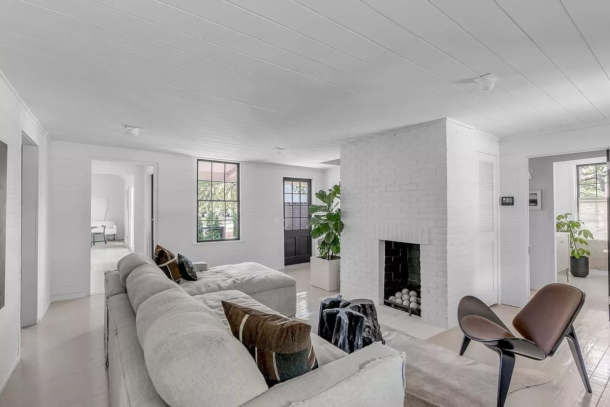 Living room with beige sofa, black accent chair, white brick fireplace, and potted plants.