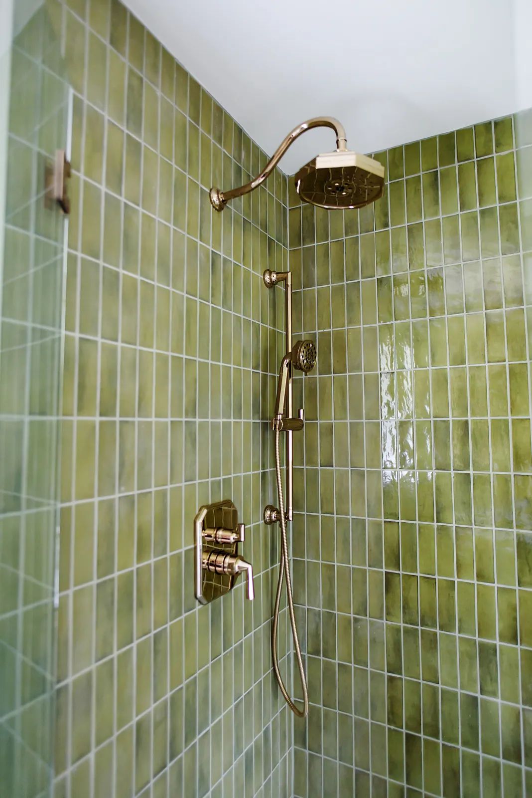 Bathroom shower with green tiles, rainfall showerhead, handheld shower, and brass control panel.