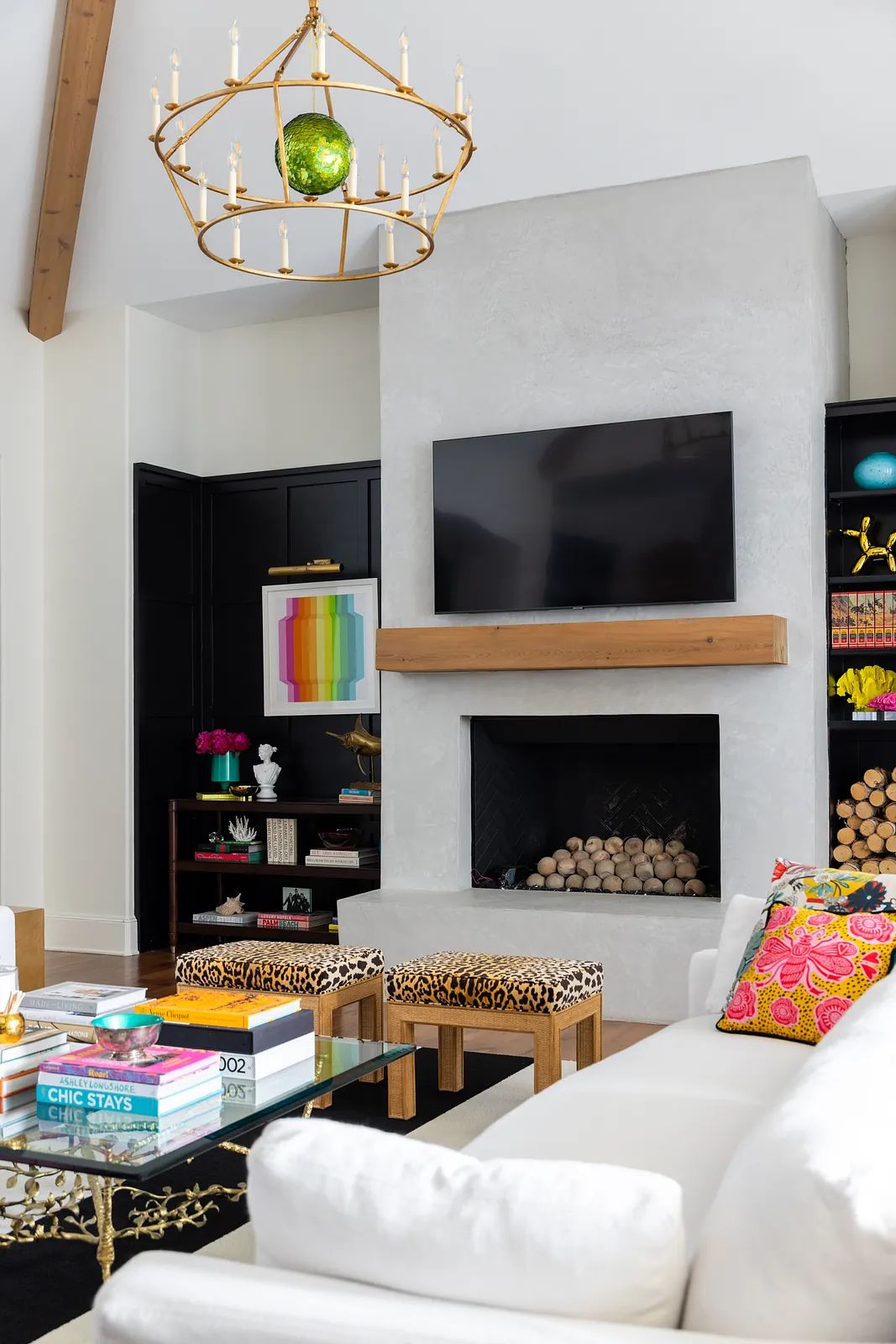 Living room with white sofa, glass coffee table, animal print stools, black shelving unit, and stone fireplace with natural light