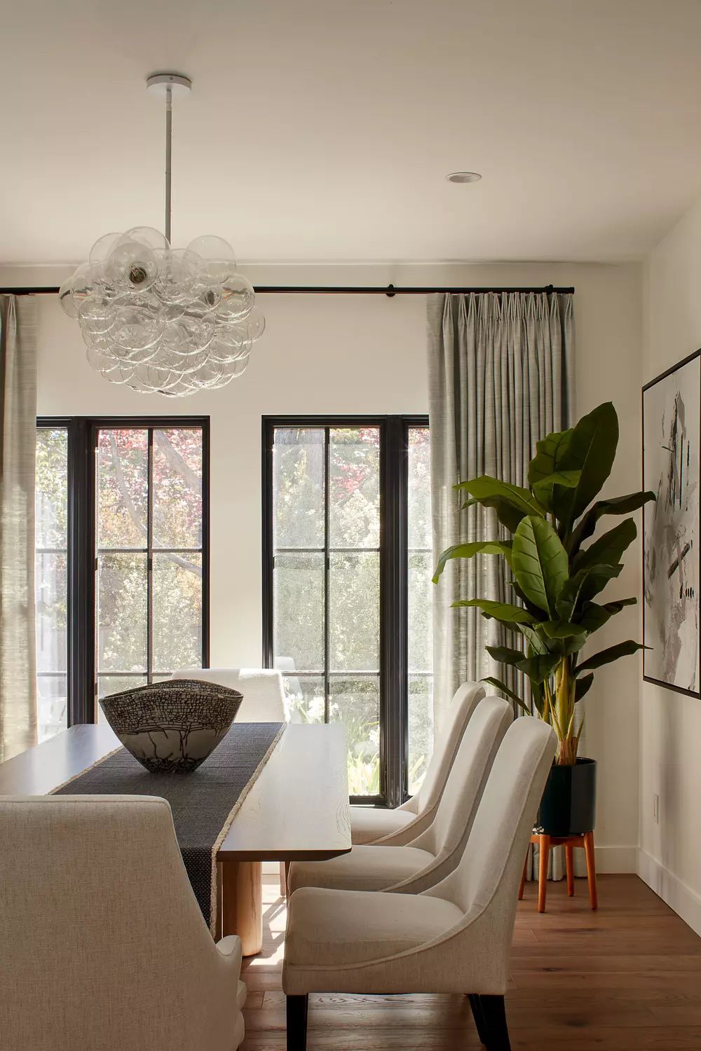 Dining room with wooden table, upholstered chairs, large pendant light, and potted plant by window