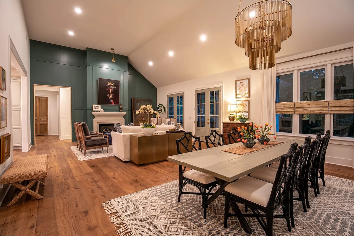 Dining room with long table, upholstered chairs, area rug, and seating area with a sofa and fireplace.
