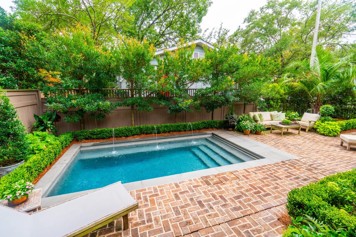 Garden with a small pool, brick paving, greenery, and lounge chairs beside the pool.