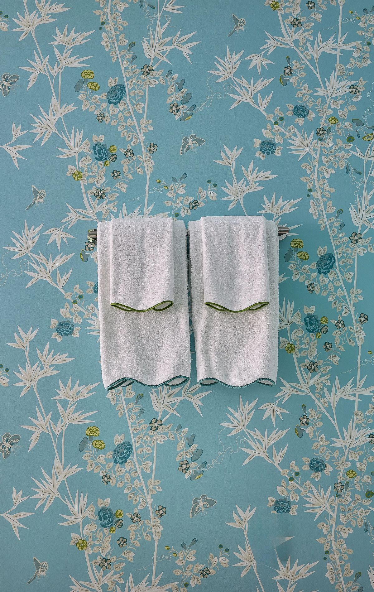 Bathroom with two white towels arranged on blue floral wallpaper.