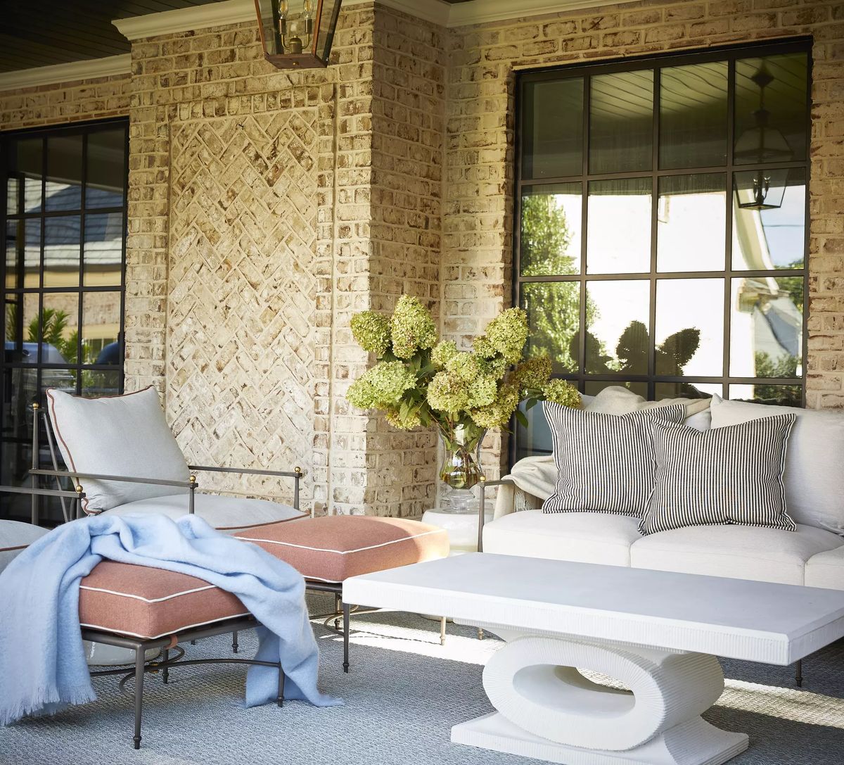 Deck with white sofa, orange lounge chair, coffee table, and vase with green flowers.