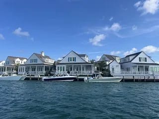 Row of waterfront houses with gable roofs, large windows, porches, and boats at docks.