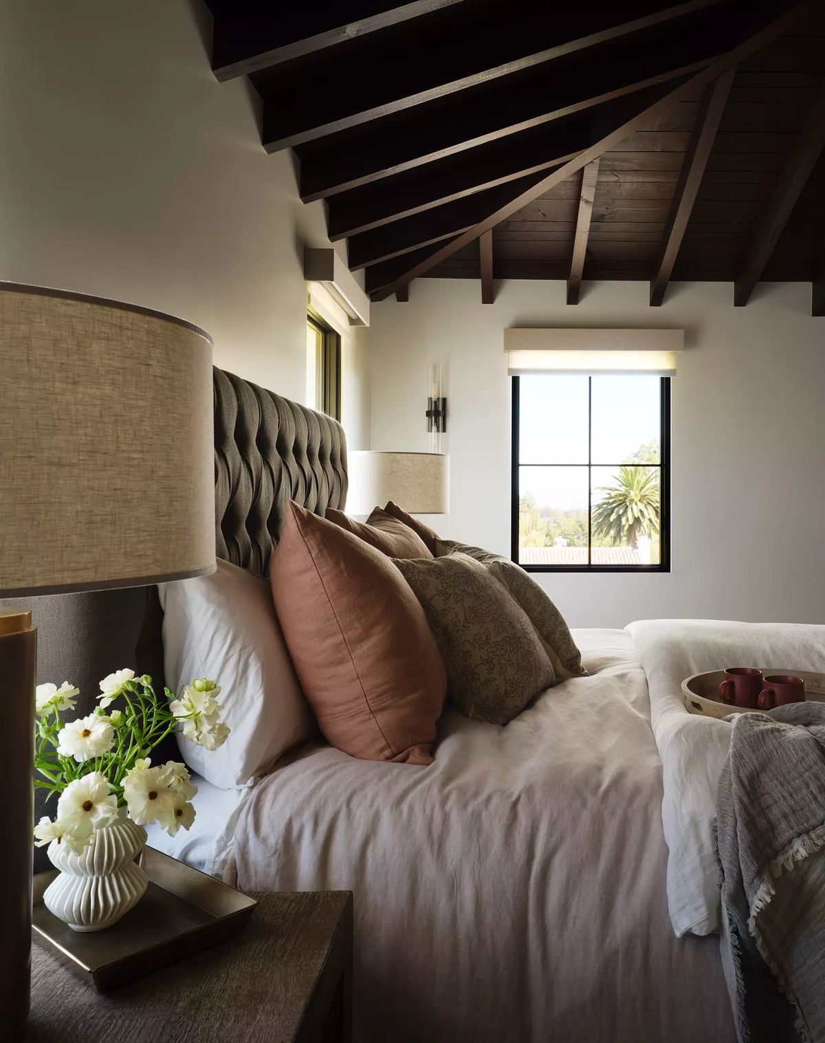 Bedroom with tufted headboard, white bedding, decorative pillows, and wooden beams on the ceiling.